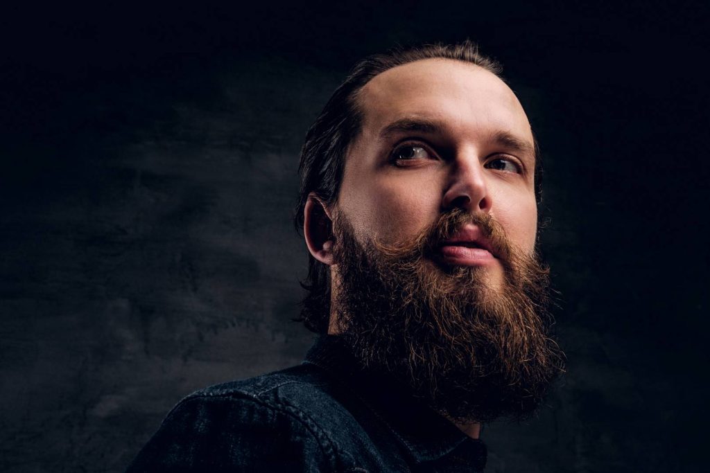 Bearded man is posing for photographer at dark photo studio.