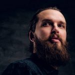 Bearded man is posing for photographer at dark photo studio.