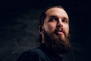 Bearded man is posing for photographer at dark photo studio.